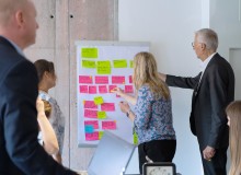 Teilnehmende eines Workshops kleben bunte Notizzettel an ein Whiteboard und diskutieren die Inhalte