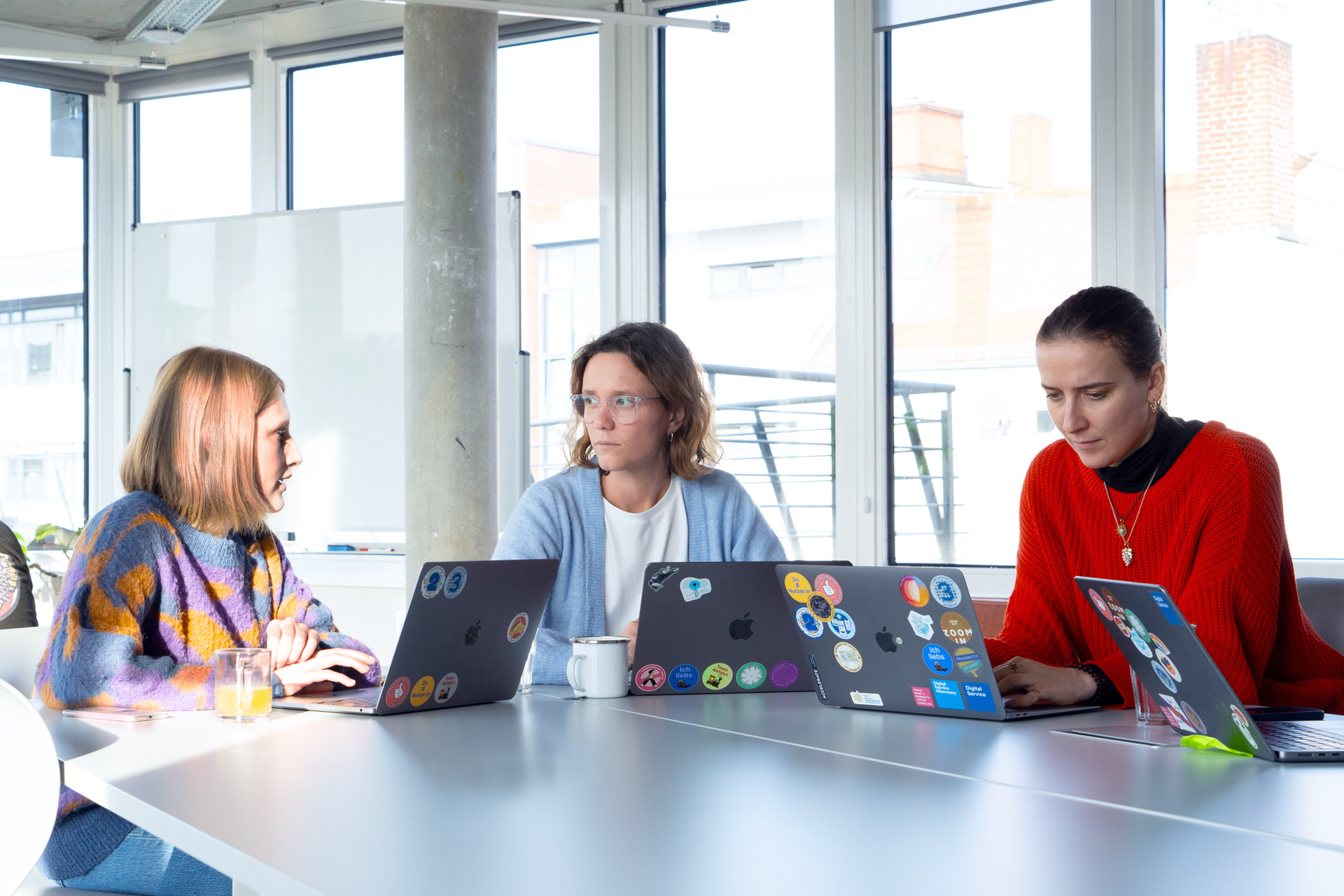 Drei Mitarbeitende des DigitalService sitzen mit ihren Laptops zusammen an einem großen Tisch im Büro.