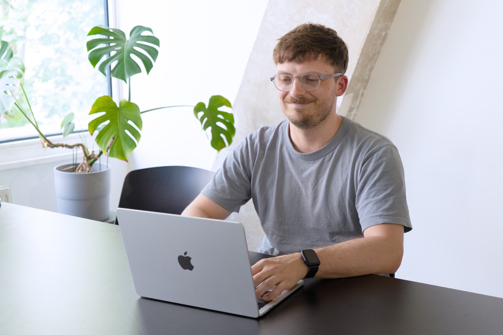 Benjamin, Principal Transformation Manager, sitzt lächelnd an einem Tisch vor seinem Laptop