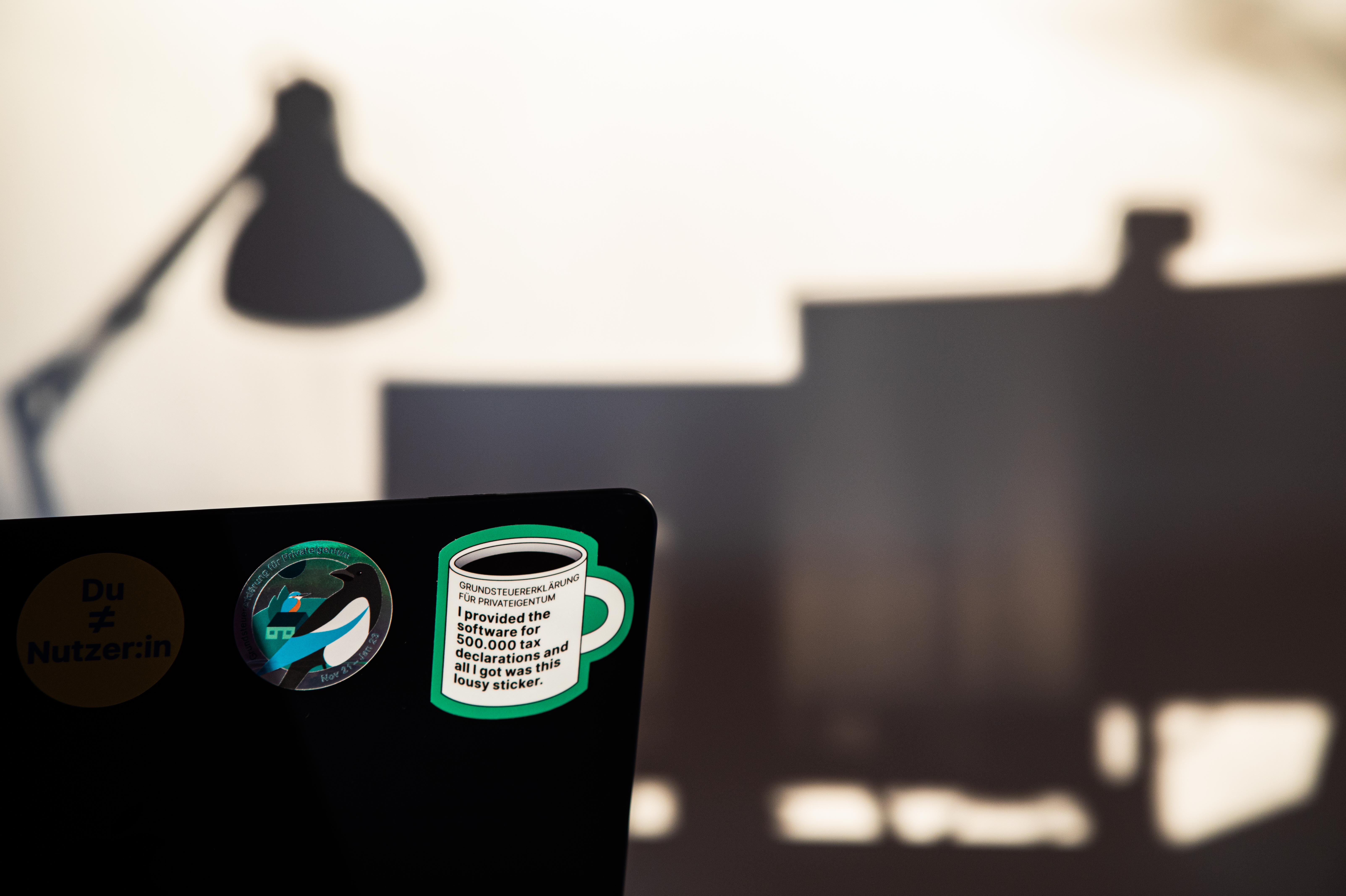 Auf der Rückseite eines Laptops kleben zwei Sticker, die für das Grundsteuer-Team designed wurden.