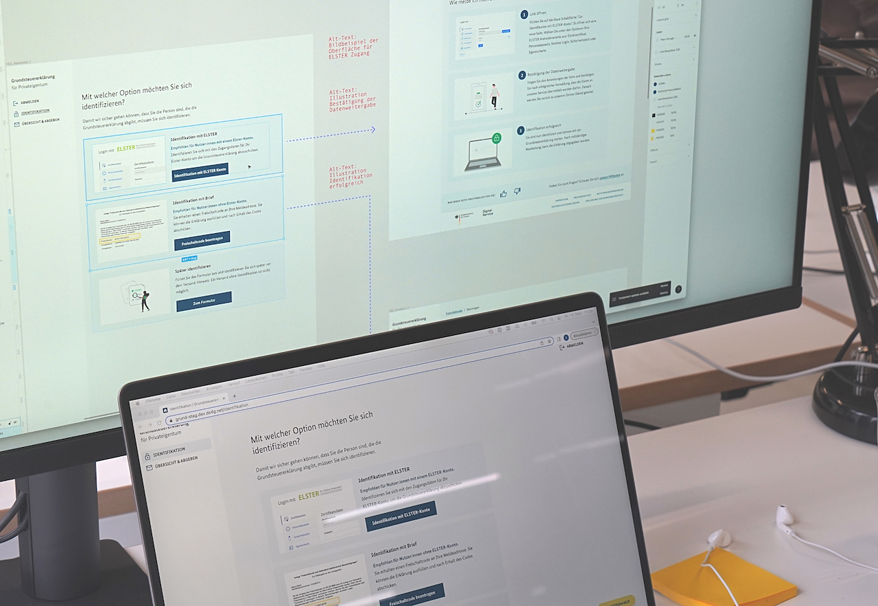 Ein Laptop steht vor einem deutlich größeren Computerbildschirm; auf beiden Geräten sind die Anmeldemöglichkeiten für den Online-Service „Grundsteuererklärung für Privateigentum“ zu sehen; auf dem Laptop in der Ansicht für Nutzende und auf dem Bildschirm in der Skizzenform für Entwickler:innen
