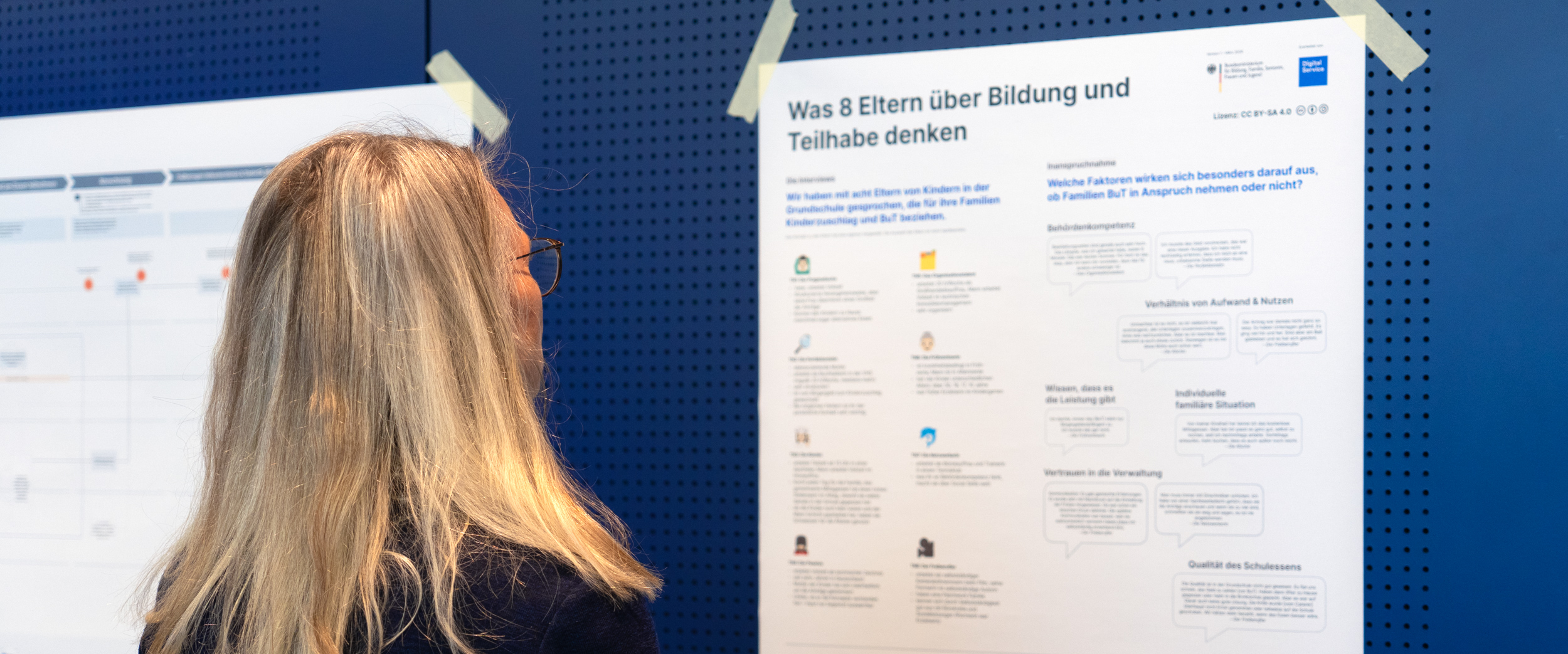 Eine Frau betrachtet ein Poster, das Ergebnisse der Nutzendenbefragung zu Bildungs- und Teilhabe-Leistungen zeigt.