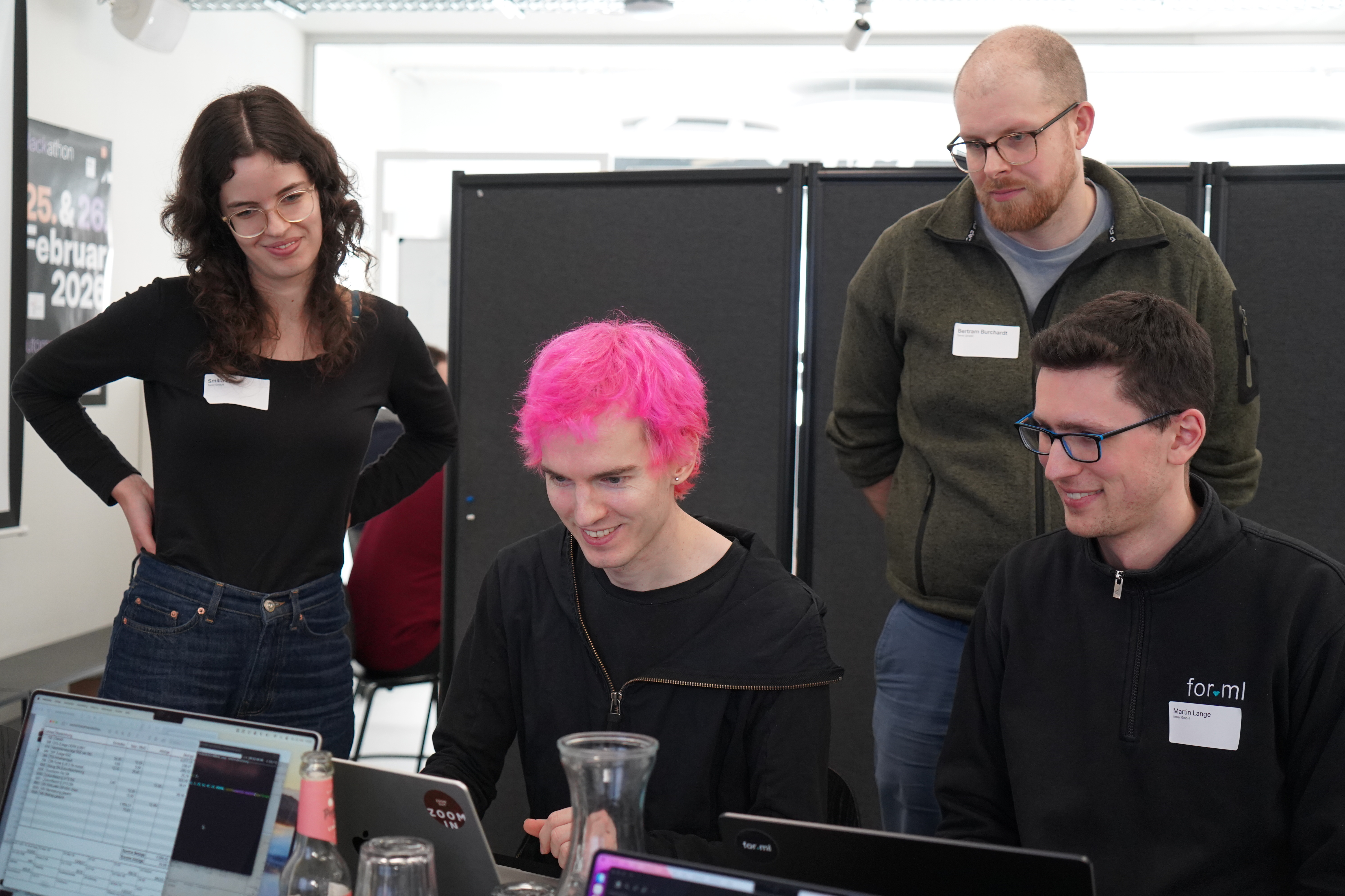 Vier Personen arbeiten gemeinsam an einem Laptop; eine Person tippt lächelnd, während die anderen zuschauen.