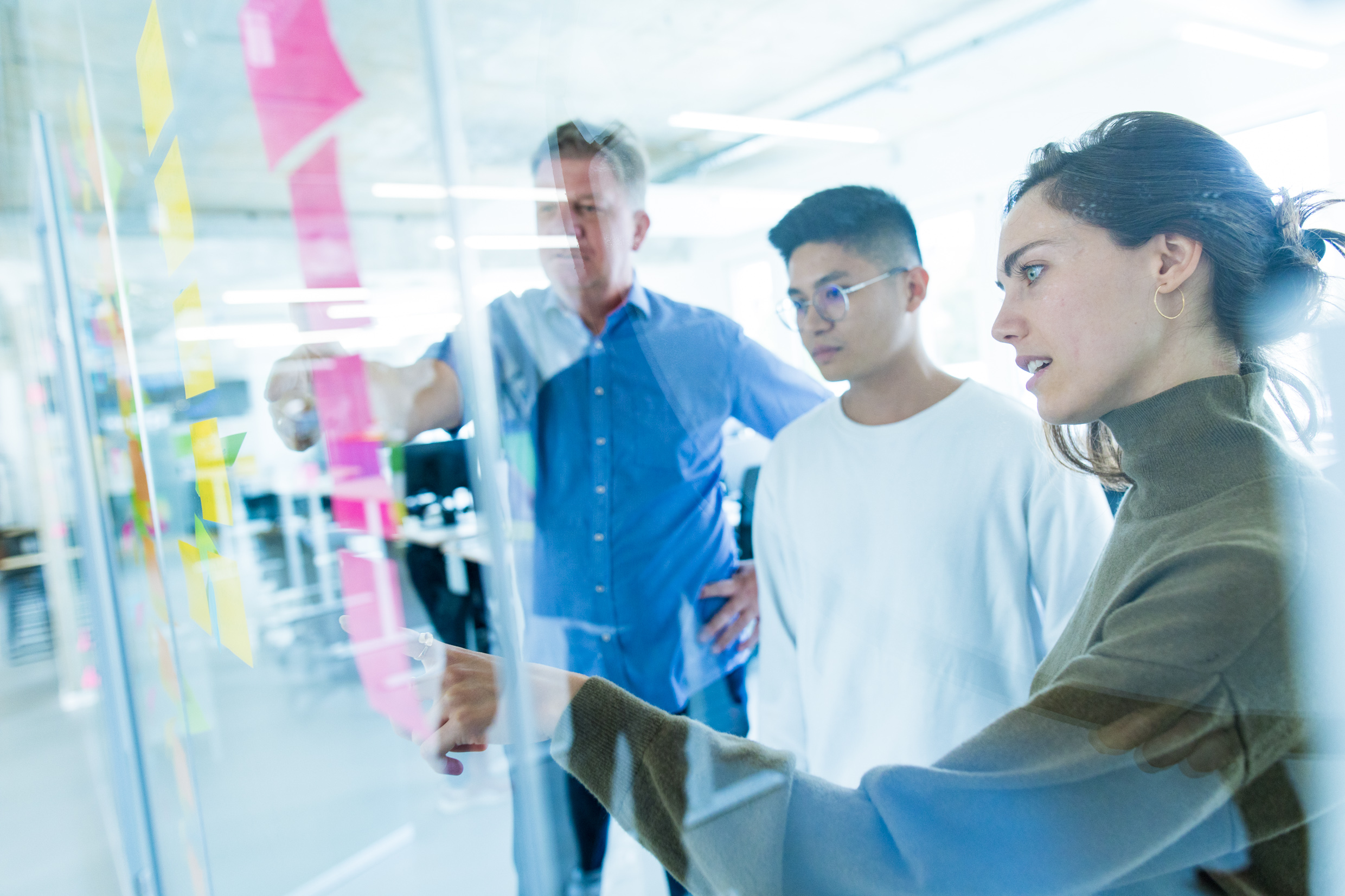 Three DigitalService employees stand in front of a glass wall in the office and brainstorm together