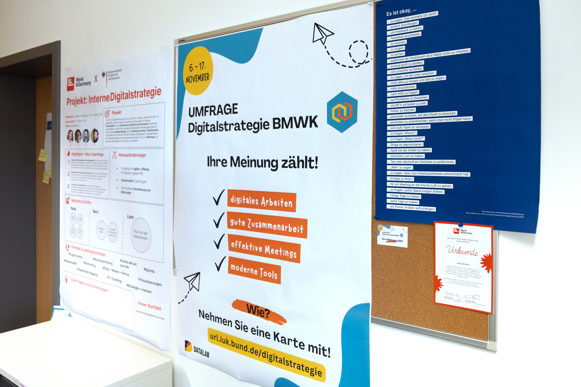 An der Wand im Büro des BMWK sind verschiedene Poster zu sehen, unter anderem eines zur Umfrage, an der Julia und Önder gearbeitet haben