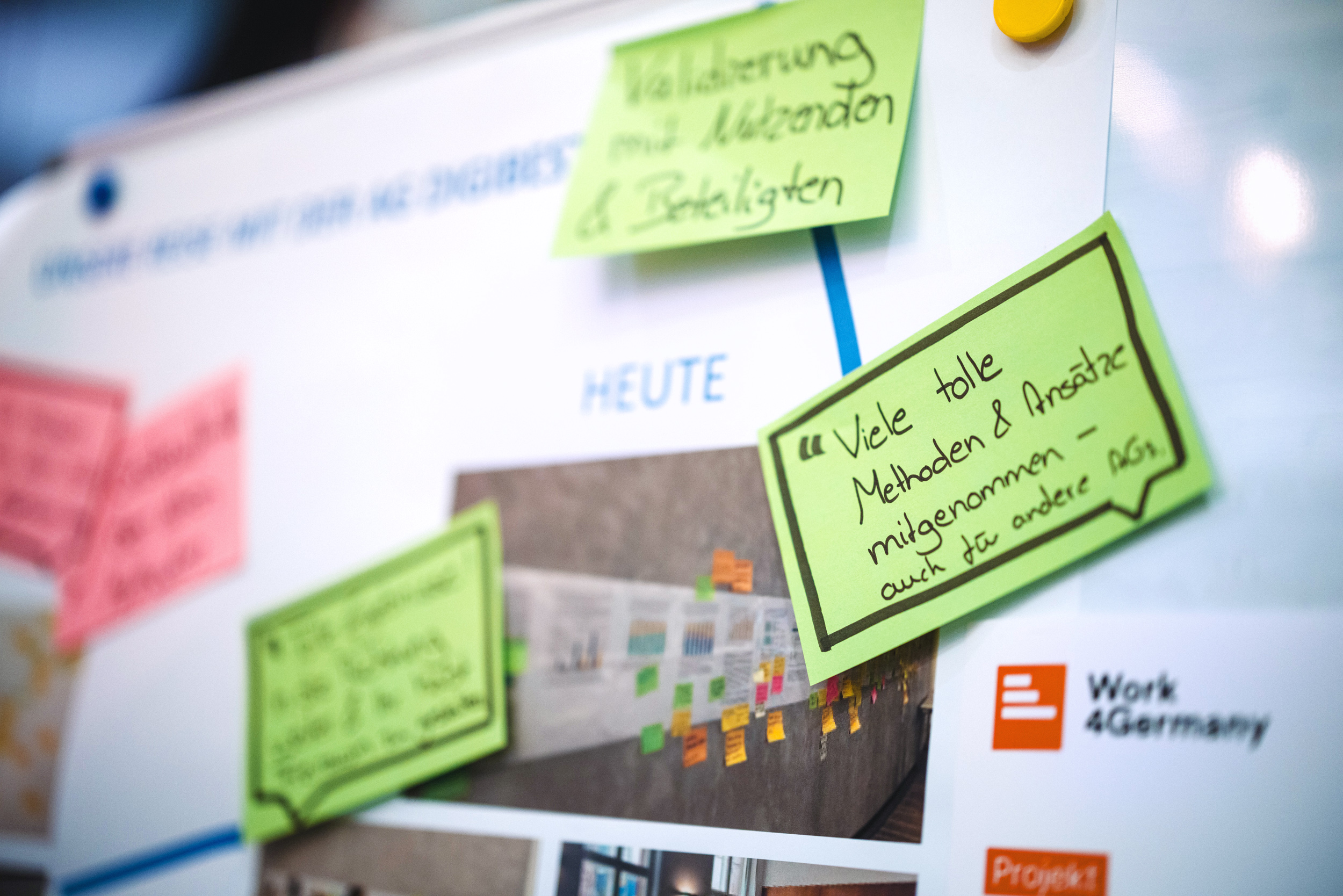 Ein Whiteboard mit mehreren bunten Haftnotizen. Eine grüne Haftnotiz im Vordergrund enthält eine handgeschriebene Notiz auf Deutsch: „Viele tolle Methoden & Ansätze mitgenommen – auch für andere AGs“. Im Hintergrund sind verschwommen weitere Notizen zu sehen. Das Logo von „Work 4Germany“ ist unten rechts sichtbar.
