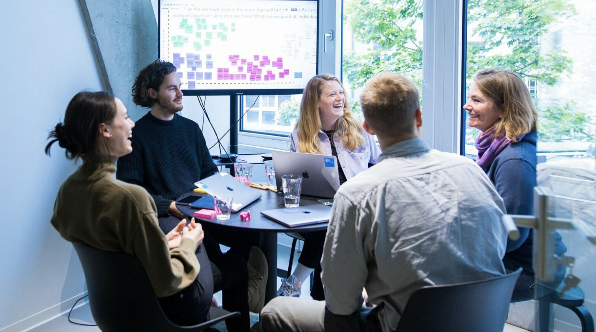 Fünf Personen sitzen am Tisch in einem Meeting