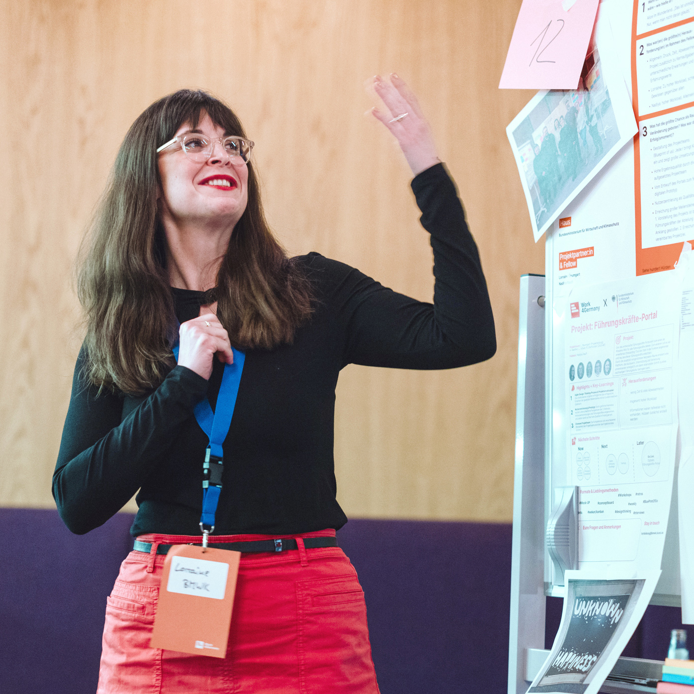 Eine Person steht vor einer Aufstellwand mit vielen Zetteln und Postern und erklärt diese gestikulierend