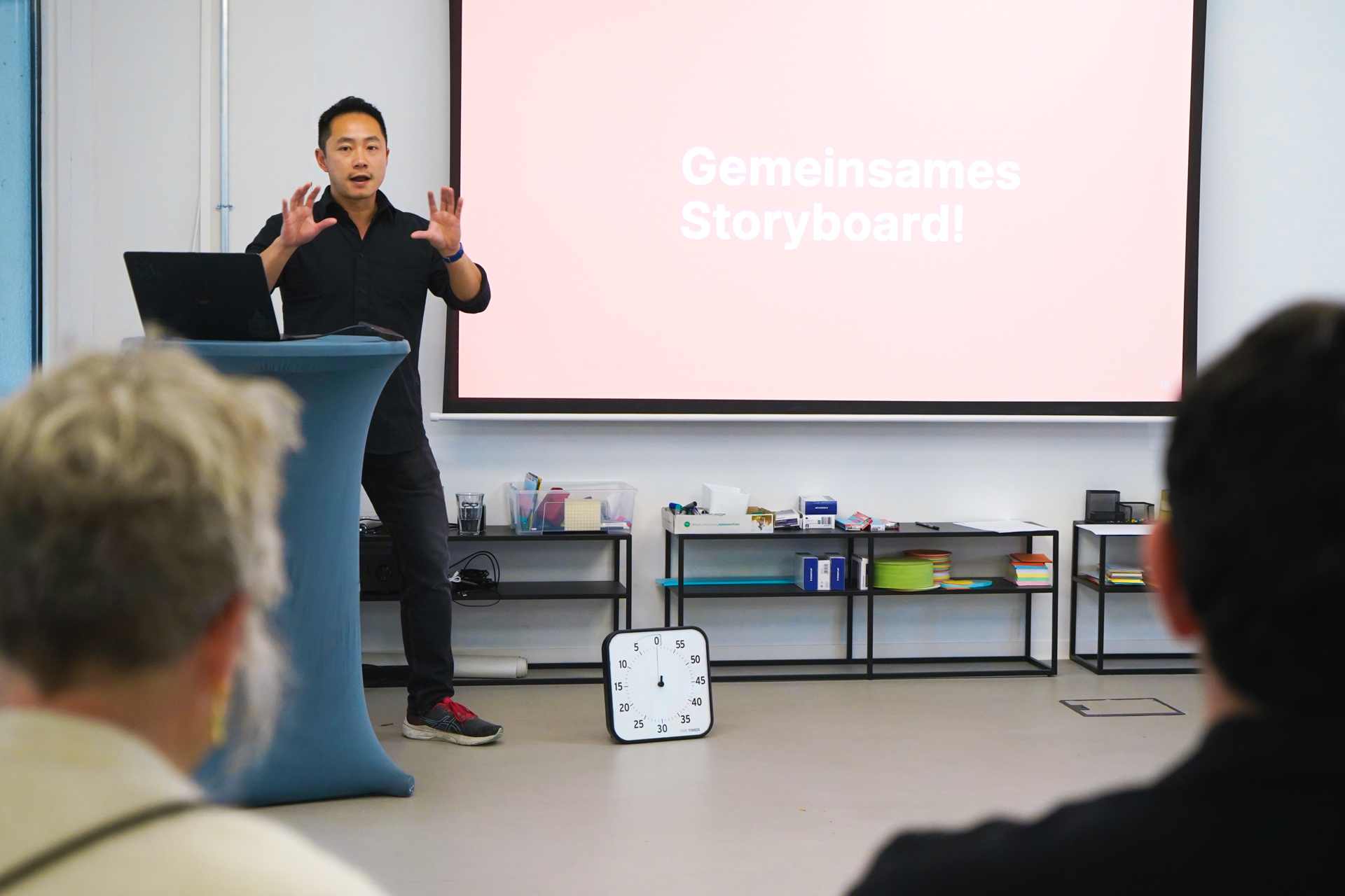 Ein Mann steht gestikulierend an einem Rednerpult; neben ihm steht auf der Folie seiner Präsentation „Gemeinsames Storyboard“