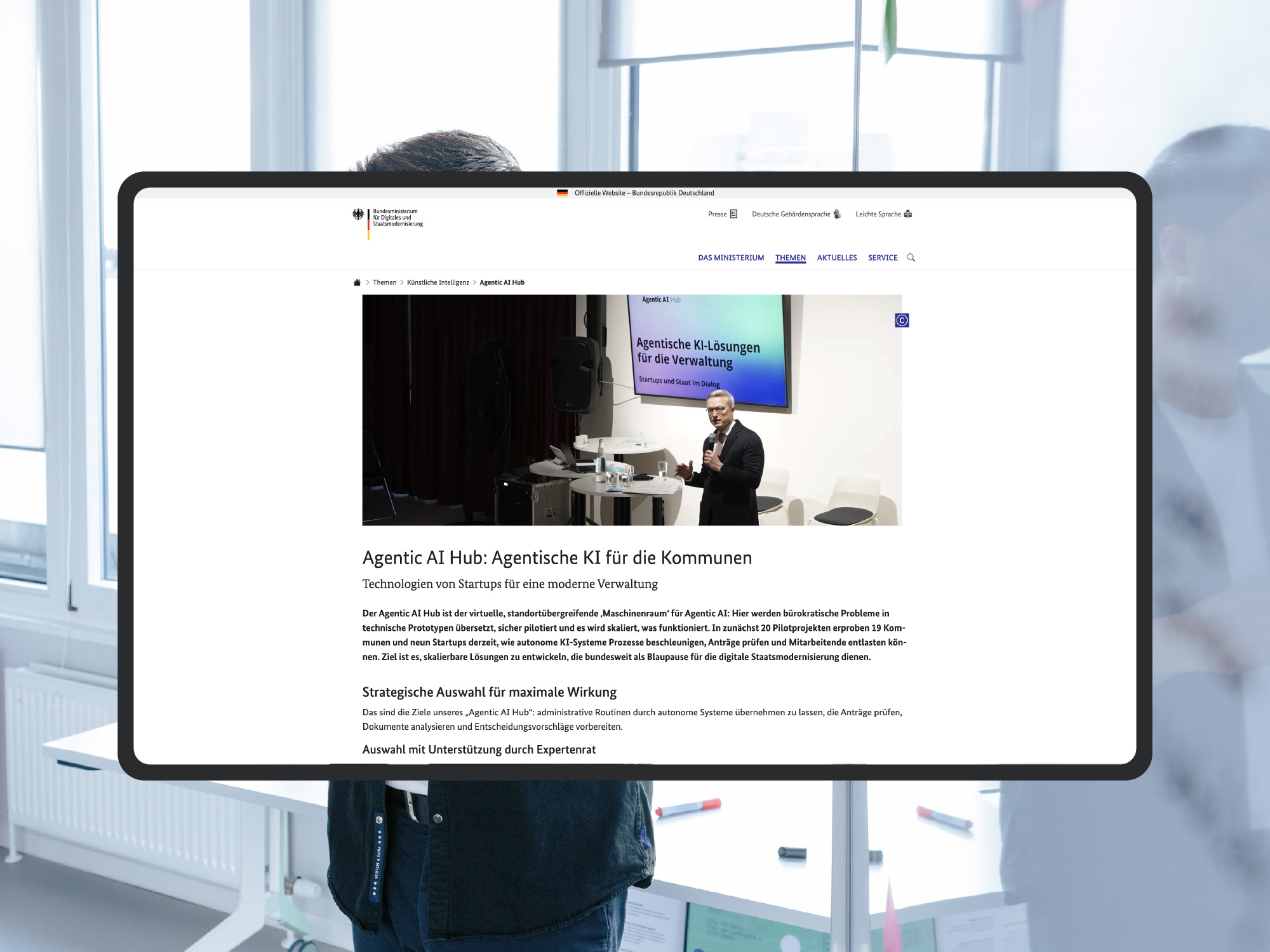 Screenshot der Webseite des Bundesministeriums für Digitales und Staatsmodernisierung zum Thema „Agentic AI Hub: Agentische KI für die Kommunen“; als visuelles Stilmittel sieht man im Hintergrund das Büro des DigitalService