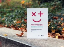 Eine Auszeichnung mit der Aufschrift „Preisträger 2024 – Preis für gute Verwaltung“ steht auf einem Steinpodest im Freien, umgeben von herbstlichem Laub.